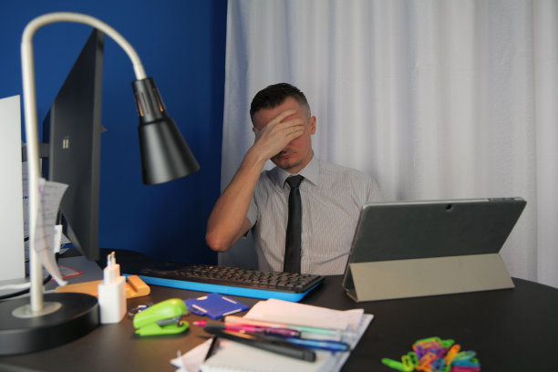 一位身穿白衬衫、系着棕色领带的年轻白人男子坐在办公室或家庭办公桌前图片下载