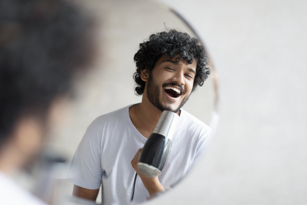 快乐的印度男人拿着吹风机，在麦克风里唱歌，在做早上美容例行公事的时候玩得很开心图片下载