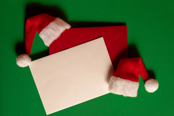 圣诞老人帽子与空纸卡注意信封上的绿色背景。复制文本空间。为广告做模特。圣诞作文图片下载