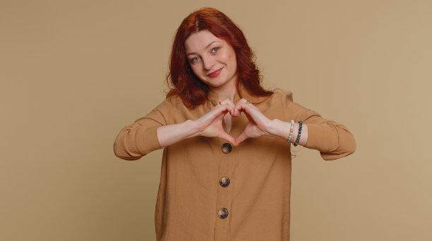 微笑的漂亮女人做心形手势，展示爱的手势，表达良好的感情和同情图片下载