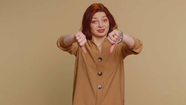 心烦意乱的年轻女子女孩在衬衫显示拇指向下的手势，不赞成，不满的厌恶图片下载