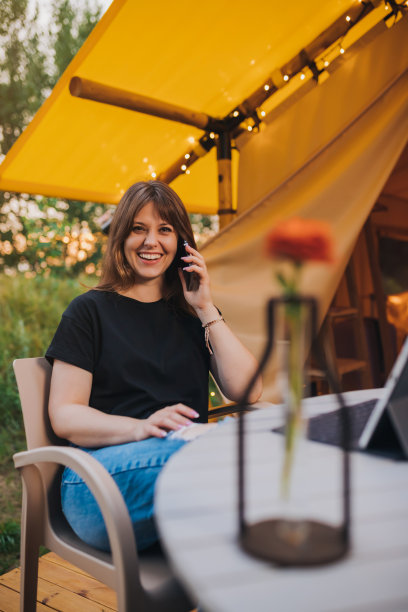 快乐的女人自由职业者在一个阳光明媚的日子里在舒适的露营帐篷里打电话和使用笔记本电脑。户外避暑度假豪华露营帐篷。生活方式的概念图片下载