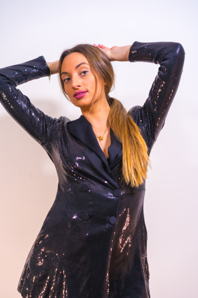 一个微笑的金发白人模特在一个黑色亮片连衣裙摆姿势在白色背景图片下载