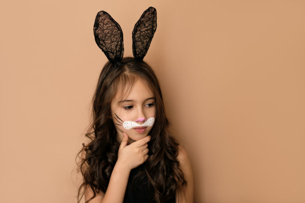 一个戴着有耳朵的帽子、画着兔子妆的孩子若有所思地看着别处图片下载