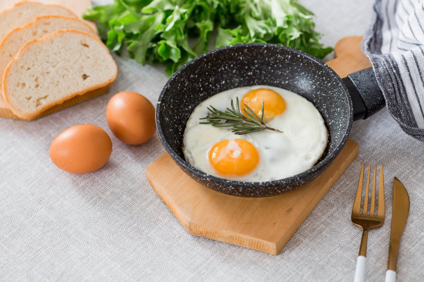 在平底锅里煎蛋，配上迷迭香、面包、鸡蛋和蔬菜沙拉，铺在亚麻桌布上。早餐，午餐和晚餐。视图是软的，选择性聚焦。乡村风格。图片下载