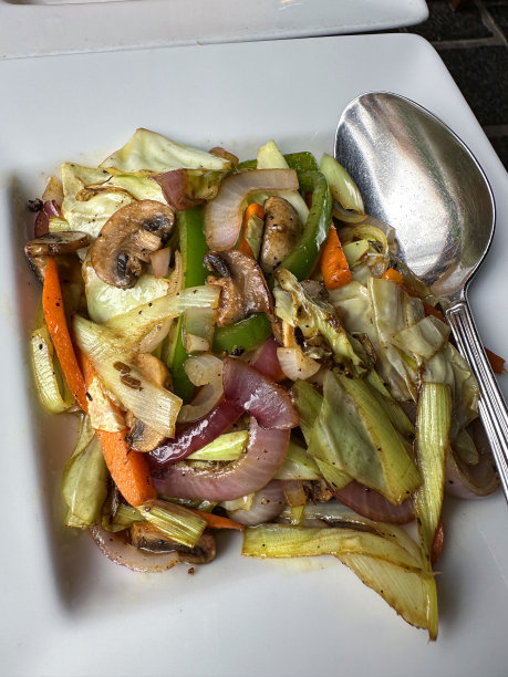 图像白色的盘子里炒着各种各样的蔬菜，白菜、胡萝卜、青椒、蘑菇、洋葱放在一个方形盘子上，用银汤匙吃，高高在上图片下载