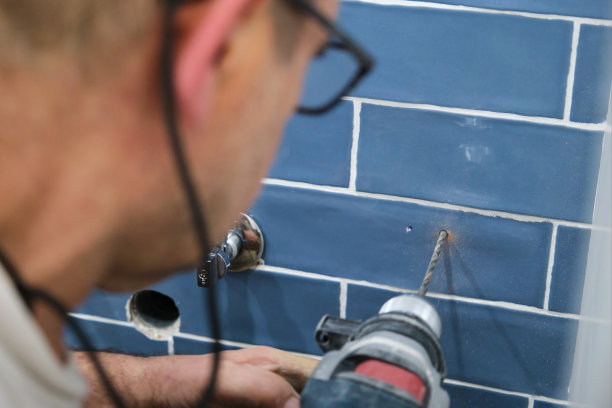 面目全非的高级泥瓦匠在瓷砖墙上钻了一个洞。图片下载