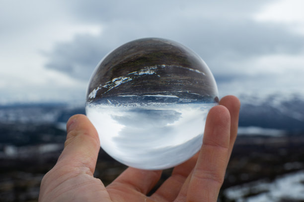 在多云的天空下，人的手拿着一个透明的球的特写图片下载