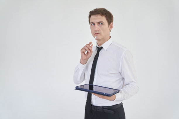 一位年轻的男性办公室职员站在明亮的背景上，手里拿着平板电脑和笔。有空间复制。高质量照片图片下载