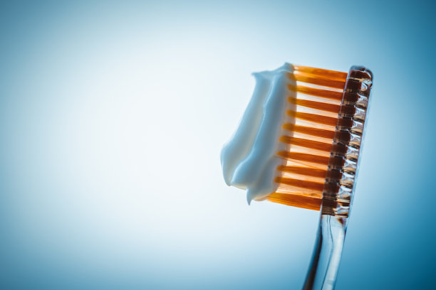 橙色塑料牙刷，蓝色背景上有白色牙膏。侧视图。副本的空间。图片下载