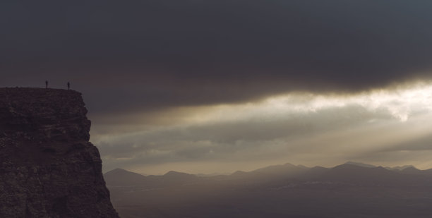 徒步旅行者站在峡谷顶端欣赏日落的全景照片图片下载