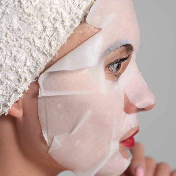 面部皮肤护理，一个年轻女子的肖像与面具在她的脸上。图片下载