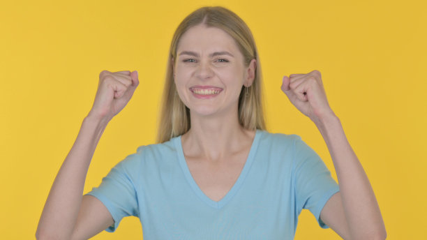 成功的年轻女子在黄色背景上庆祝图片下载