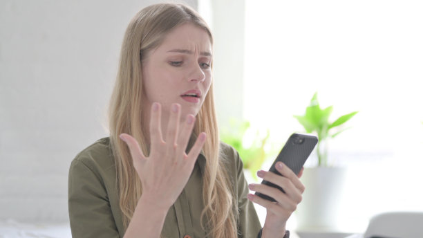 年轻的金发女子在智能手机上对失去的反应图片下载