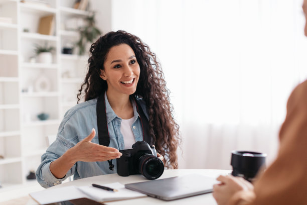 积极的摄影师与坐在现代办公室的女士交谈图片下载