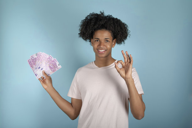 年轻的非洲裔男子拿着欧元钞票，在蓝色背景上显示OK手势图片下载