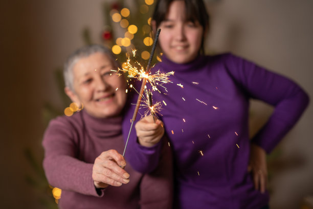 在圣诞树的背景下，人们手中燃烧的孟加拉灯。圣诞快乐，新年快乐。图片下载
