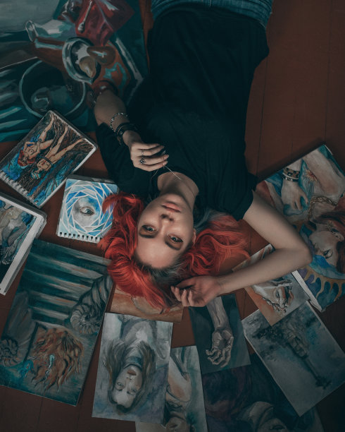年轻的红发女艺术家躺在地板上，带着她的画图片下载