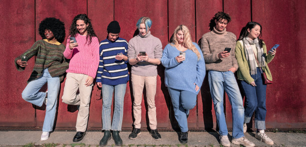 一群年轻的千禧一代站在一堵工业墙前，每个人都沉浸在自己的智能手机屏幕上。当今社会对技术依赖的概念图片下载