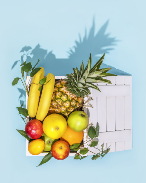 新鲜成熟的热带水果，叶子放在蓝色背景的木盒里图片下载