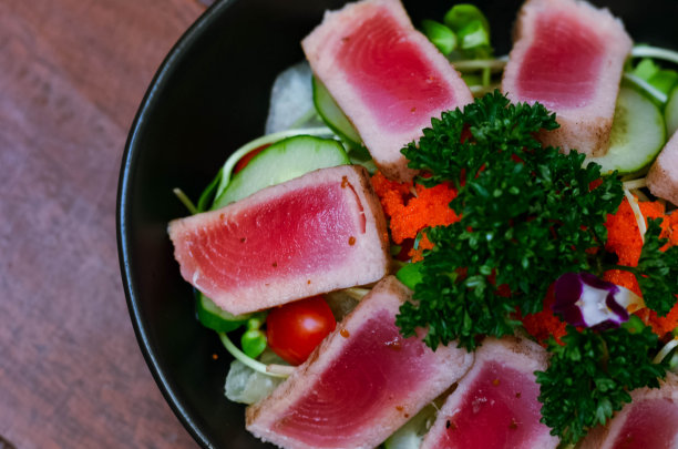 新鲜的金枪鱼沙拉配上向日葵芽和新鲜的有机生菜，装在一个优雅的黑色盘子里，放在木桌上，还有旧报纸。图片下载