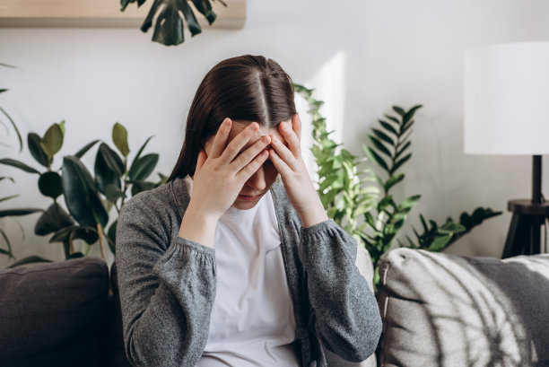 忧心忡忡的年轻女子想要克服坏的生活事件，思考艰难的决定。危急情况的概念。悲伤的女性坐在沙发上，身体前倾，双手合十，试图控制情绪图片下载