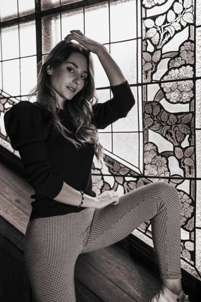 一个女人坐在玻璃窗前的木楼梯上的灰度垂直镜头图片下载