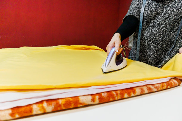 一位女裁缝正在用蒸汽熨斗熨烫彩色布料。图片下载