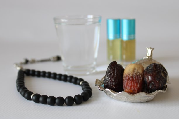 白色背景上的麦地那蜜枣、渗渗泉水、黑色念珠和香精油。斋月主题照片。图片下载