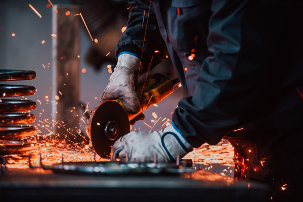 穿着特殊衣服和护目镜的锁匠在生产中工作。用角磨床进行金属加工。金属加工的火花。图片下载