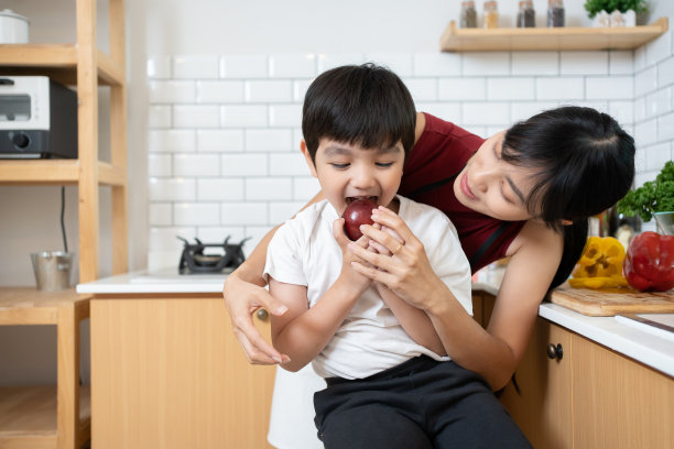 亚洲小孩和妈妈在厨房啃苹果。迷人的妈妈教导和支持年轻的男孩女儿照顾他的牙齿，吃水果醒来后在家里进行保健。图片下载