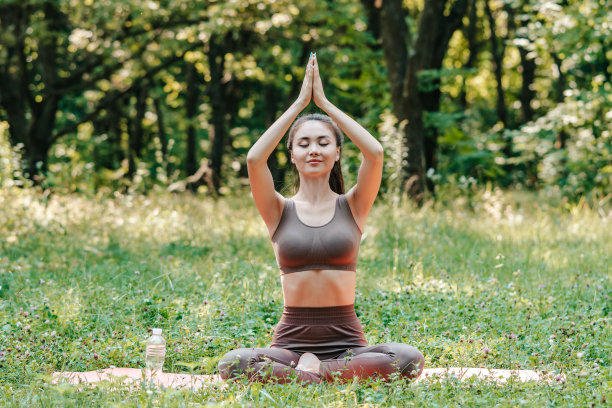 平静的年轻亚洲女子在户外练习瑜伽，坐在莲花姿势。通过冥想来达到内心的和谐与平衡。森林草地上的宁静气氛。图片下载