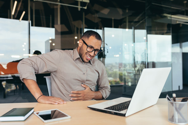 商人在办公室生病，戴眼镜的人严重胃痛，非裔美国人在大楼里使用笔记本电脑工作图片下载