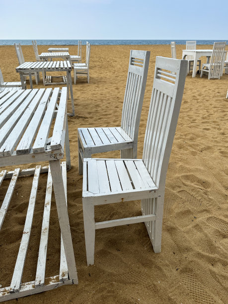 在斯里兰卡科伦坡的拉维尼亚山海滩上，乡村的木制板条餐桌特写图像，一组白色的木制桌椅，为游客提供露天用餐区，蓝色的天空和大海背景，重点放在前景图片下载