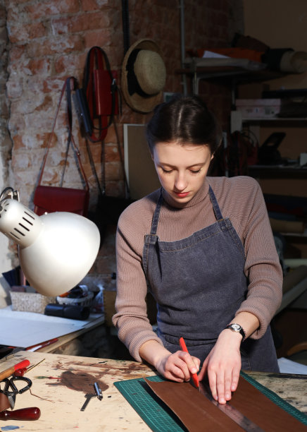 年轻的黑发女人在一个包制作工作室工作图片下载