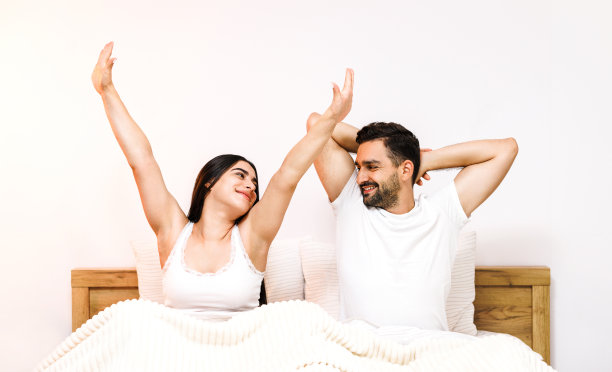 早上，年轻可爱的夫妇在睡了一觉后，在家里的床上伸展身体。图片下载