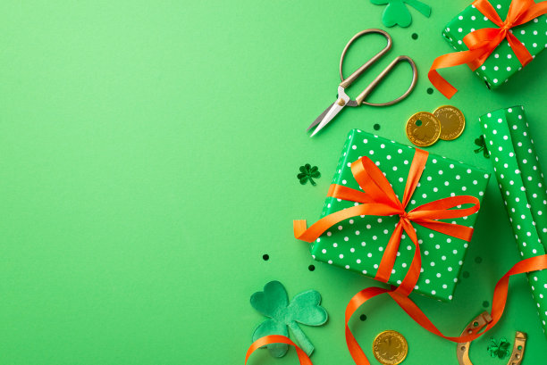 圣帕特里克节的概念。顶部视图照片绿色礼品盒与橙色丝带蝴蝶结包装纸剪刀金币三叶草马蹄形纸屑孤立的绿色背景与复制空间图片下载