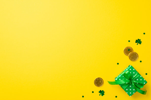 圣帕特里克节的概念。顶部视图小绿色礼品盒在包装纸与波点图案和弓金币和三叶形纸屑孤立的黄色背景与空白的照片图片下载