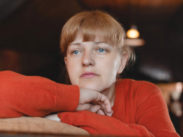 一个穿着毛衣的金发白人女人很悲伤，她的头靠在手上，悲伤地看着一边。在室内。低角度视图。图片下载