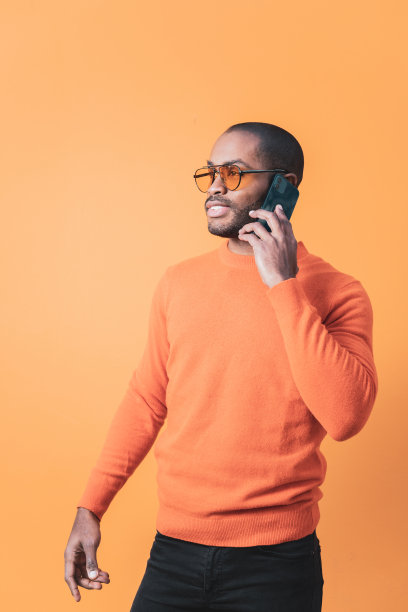 这是一名英俊的哥伦比亚男子用手机打电话的照片，他穿着与背景颜色相同的衬衫。橙色背景。图片下载