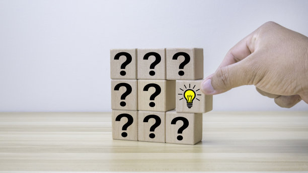 问号和创意概念。手拿一个木立方体，上面画着一个灯泡和一排在木头背景上有问号的立方体。图片下载