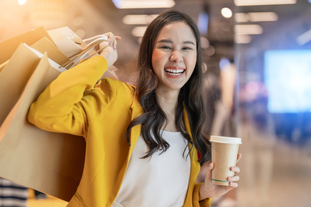 令人惊讶的开朗的亚洲女性成年女性购物者手拿购物袋和咖啡纸杯走在百货商店购物中心买衣服与幸福退出，露齿微笑快乐图片下载