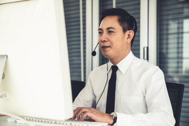 商人戴着耳机在办公室积极工作。呼叫中心、电话营销、客服为客户提供电话视频会议服务。图片下载