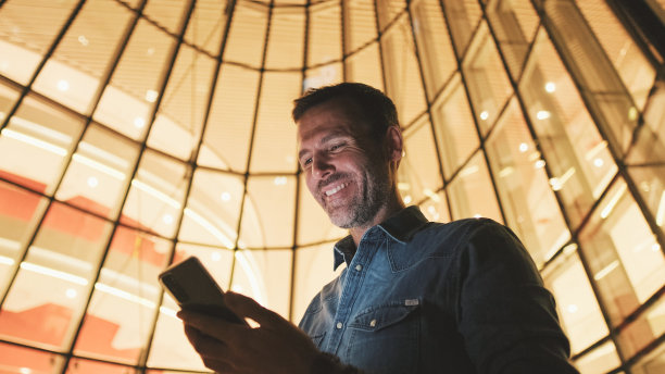 特写，中年男子晚上站在商业中心旁边使用手机图片下载