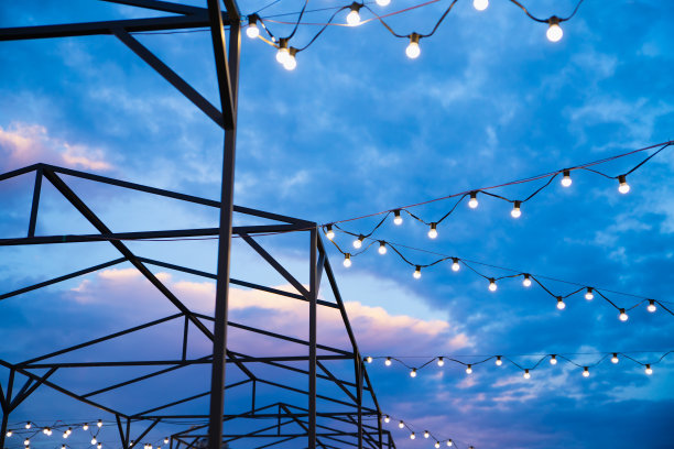 灯管装饰和遮阳篷结构的户外活动，派对，音乐会，节日，游乐场。夜晚多云的天空上，街道外亮着灯泡的花环。图片下载