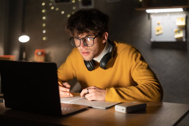 帅气的阿拉伯大学生在笔记本电脑上学习，晚上坐在宿舍里写笔记。图片下载