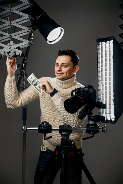 摄影师，三脚架上的数码相机，手里拿着百元大钞图片下载