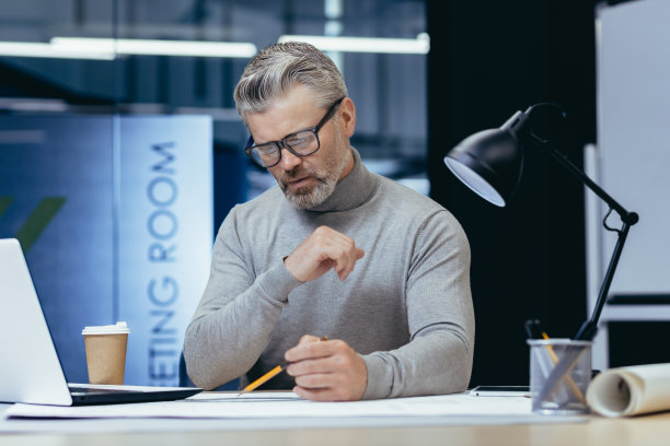 高级男建筑师晚上集中在办公室的一盏灯前工作。绘制平面图图片下载