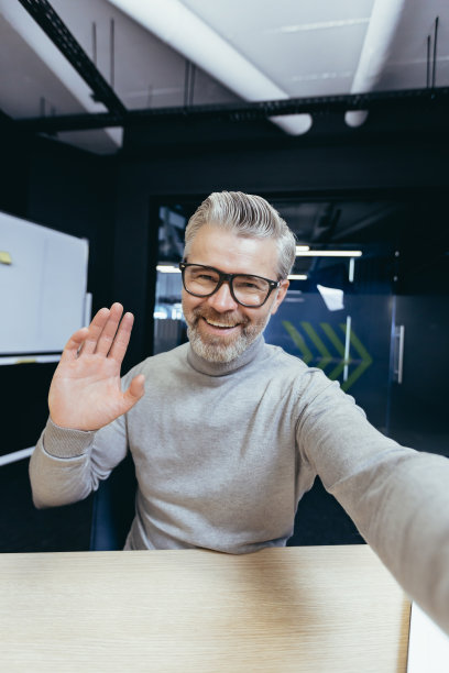 成熟的男人在办公室里用手机上的应用程序进行视频通话，高级商人与朋友和同事愉快地交谈，自拍照片图片下载