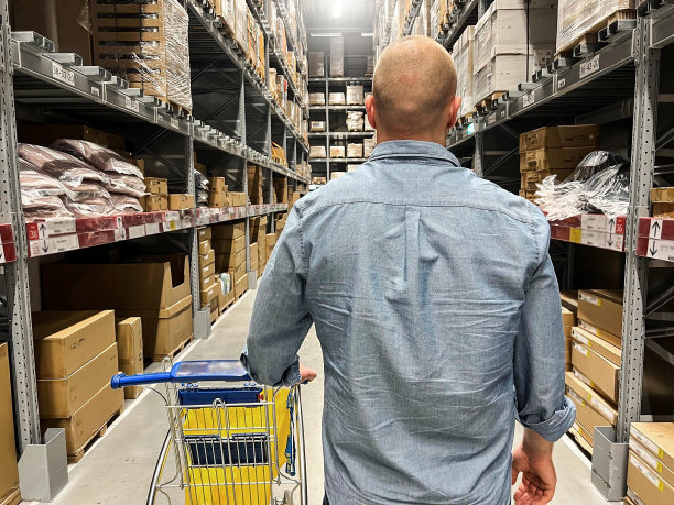 裁剪的年轻白人快乐的人使用手推车把纸箱里面。在仓库采购家具。仓库大存储或货物分配和人的背部与购物车。图片下载